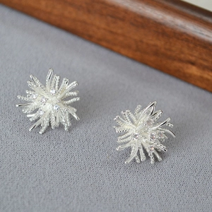 Close-up of radial silver firework earrings with micro-set zircon on textured grey cloth