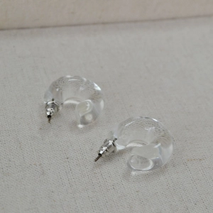 Transparent C-shaped resin hoop earrings with metal posts on cream textured fabric background