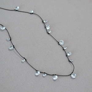 Dettaglio di elegante collana in cordino nero con ciondoli a fiore in cristallo lucido
