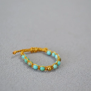 Détail d'une bague bohème en perles turquoise faite main avec cordon tressé jaune et perle dorée
