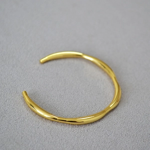 Macro detail of irregular wave textured gold-plated brass cuff bracelet with mirror finish