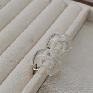 Detailed view of clear glass C-shaped drop earrings on a beige linen jewelry tray