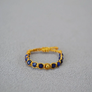Détail d'une bague tissée main avec perles de lapis bleu et une perle dorée