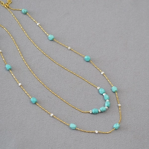 Detail view of gold beaded chain with faceted turquoise gemstones in a retro layered style