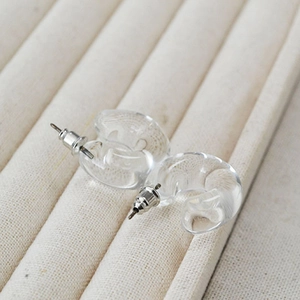 Macro shot of minimalist clear C-shaped resin earrings on a beige velvet jewelry stand