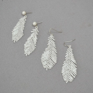 Macro detail of handmade white beaded feather earrings with pearls and silver hooks