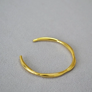 Minimalist gold brass open cuff bracelet with irregular wavy lines on grey fabric