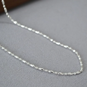 Close-up of polished silver olive-shaped beads and textured chain link necklace