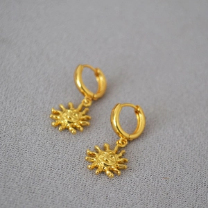 Minimalist brass gold plated sun face huggie hoop earrings on a grey textured background