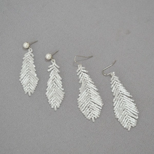 Detailed view of handmade white glass bead earrings with feather shape and pearl accents