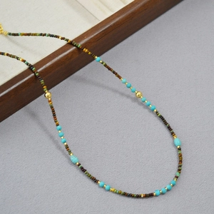 Bohemian beaded necklace with turquoise and gold accents on a wooden display stand