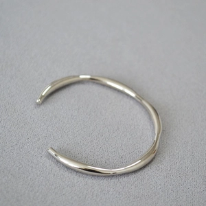 Macro shot of polished silver brass cuff showing irregular fluid lines and modern textures