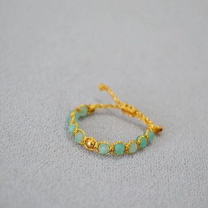 Gros plan d'un bracelet tissé en fil d'or avec perles turquoise et perle centrale dorée