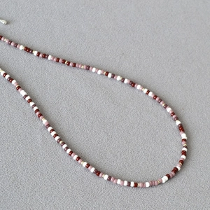 Detail of bohemian red and ivory beadwork with silver clasp on textured grey fabric