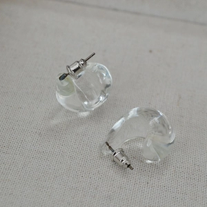 Macro shot of minimalist clear glass C-shaped stud earrings on white textured fabric