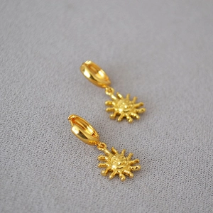 Detail of gold-plated sun drop earrings featuring intricate facial engravings and glossy finish