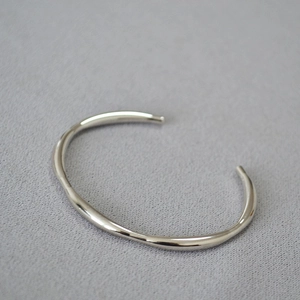 Detailed macro view of silver irregular wavy open bangle with polished metallic finish
