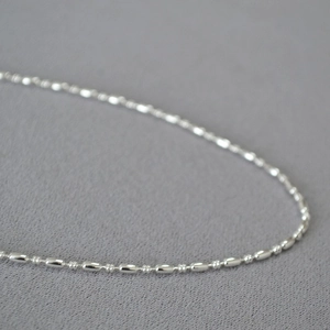 Close-up of polished silver rice bead chain necklace with smooth cylindrical links