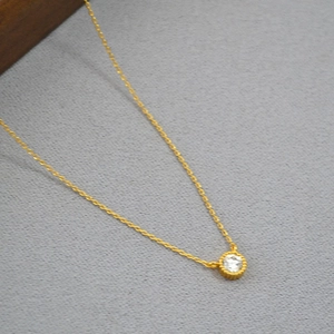 Macro view of gold plated brass necklace featuring a round zircon with radiating gear edge