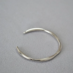 Minimalist silver wavy open bangle with irregular curved lines on grey texture