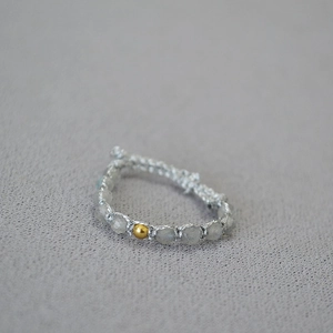 Gros plan d'une bague tressée à la main avec des pierres grises et une perle dorée