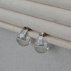 Macro detail of clear glass teardrop C-shaped stud earrings on beige fabric display