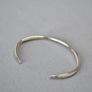 Detailed view of silver wavy bangle with irregular thickness and mirror-polished finish