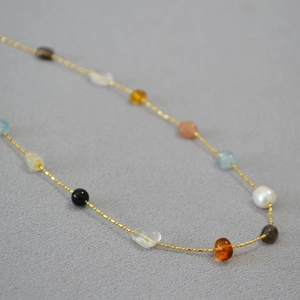 Macro view of dainty gold chain necklace with colorful crystals and pearl beads