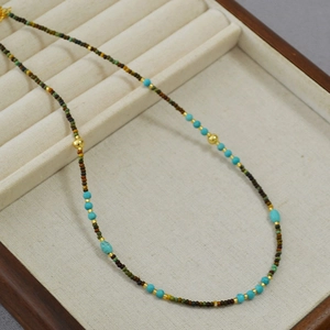 Close-up of bohemian beaded necklace with turquoise and gold accents on a jewelry tray
