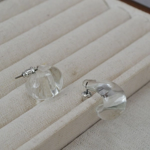 Macro shot of minimalist clear teardrop C-shape earrings on a beige jewelry display tray