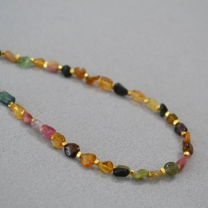 Close-up of irregular tourmaline beads with golden metal spacers on fabric