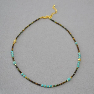 Vintage style beaded necklace with turquoise stones and golden accents on a gray background