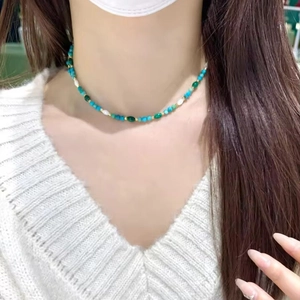 Detail view of a beaded necklace with turquoise, dark green beads and white pearls on a model
