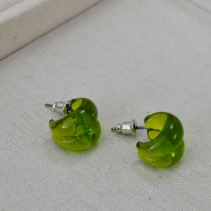 Detail view of translucent grass green C-shaped resin stud earrings on fabric background