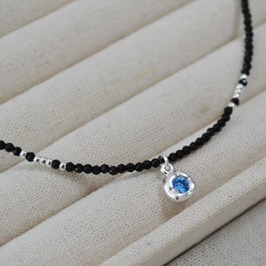Macro detail of black beaded necklace with a round blue gemstone pendant on beige velvet