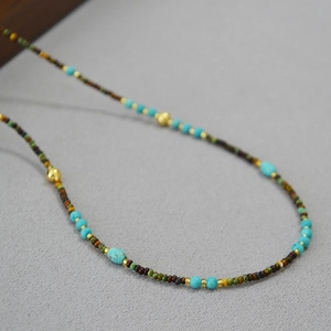 Detail of beaded necklace with turquoise stones and golden accents on textured fabric