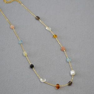Close-up of gold chain necklace with colorful irregular gemstones and single pearl