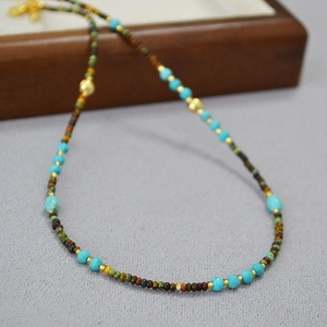 Detail of beaded necklace with turquoise stones and gold accents on textured surface
