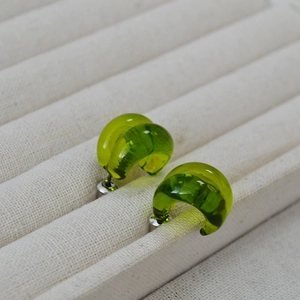 Detail of grass green C-shaped translucent glass stud earrings on a beige tray