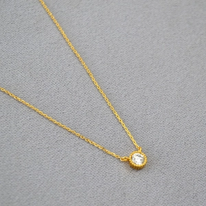Minimalist gold plated brass necklace with a sparkling round zircon pendant on a grey fabric