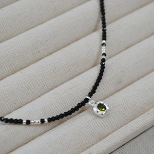 Close-up of black beaded necklace with a green zircon pendant in silver bezel setting
