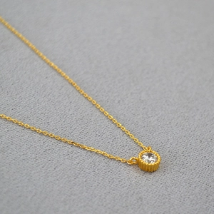 Detailed view of single round-cut zircon pendant with gold-plated bezel on fine link chain