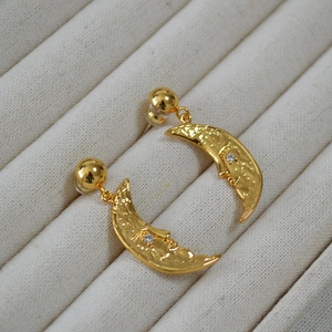 Detail of moon-shaped gold brass earrings with textured face and inlaid zircon