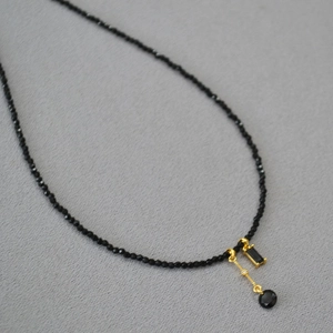 Gros plan du collier en perles de spinelle noire avec pendentifs géométriques dorés et gemmes