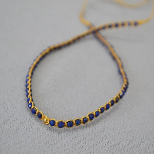 Gros plan d'un bracelet bohème avec lapis-lazuli et détails de fils dorés tressés