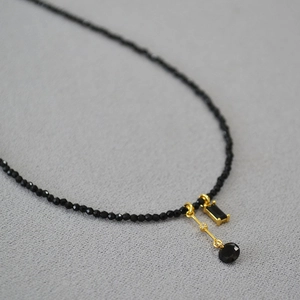 Gros plan du collier en perles de spinelle noire avec pendentif géométrique doré élégant