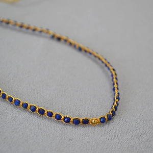 Détail macro d'un bracelet bohème tissé main avec perles de lapis et fil doré soigné