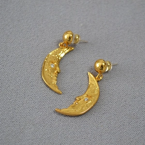 Macro detail of retro brass crescent moon earrings with human face relief and zircon