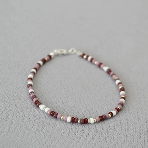 Detail of bohemian beaded bracelet with red beads and lobster clasp on grey fabric