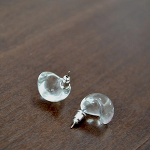 Macro detail of transparent teardrop glass earrings with silver pins on a dark wood surface